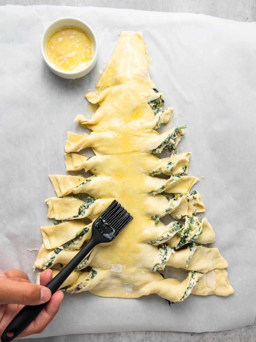 melted butter with garlic powder being brushed onto puff pastry christmas tree