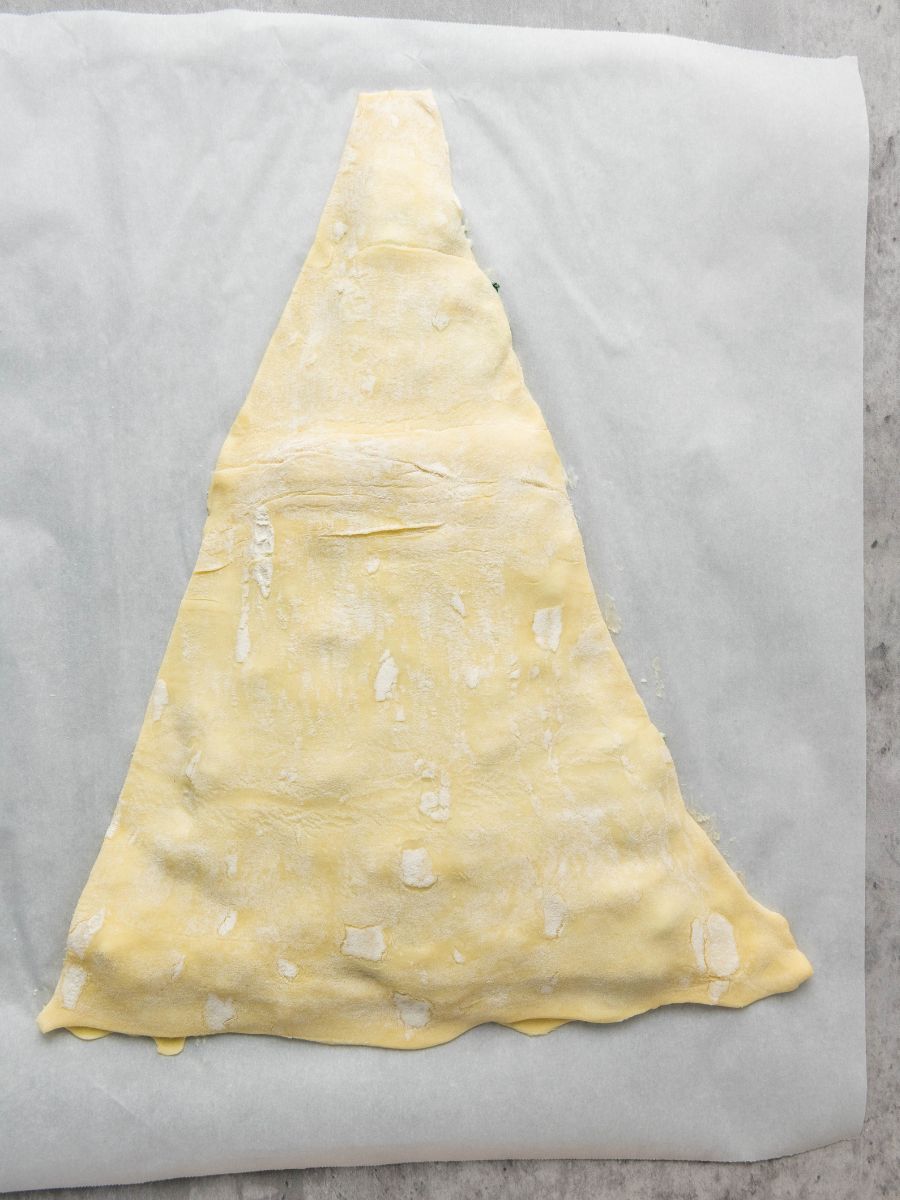 triangle of puff pastry placed over spinach dip and bottom sheet of puff pastry