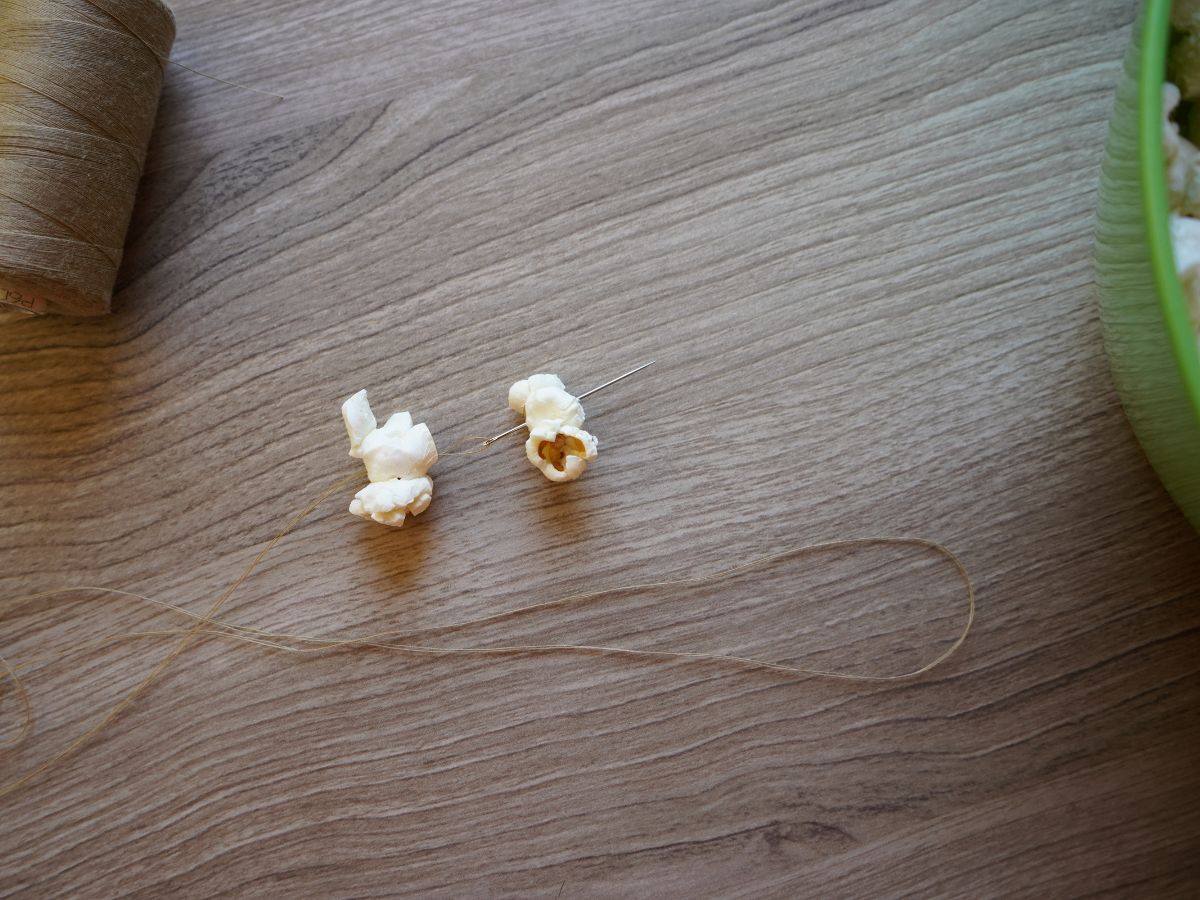 close up of thread going through two pieces of popcorn to make garland