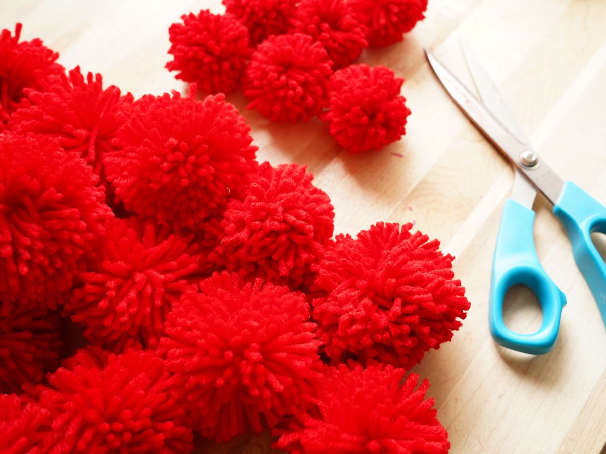 pile of red pom poms on table with pair of scissors