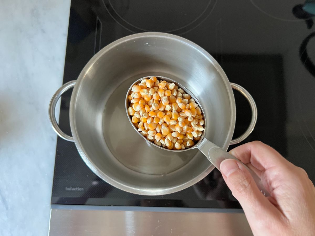 pot on stovetop with measuring cup filled with popcorn kernels