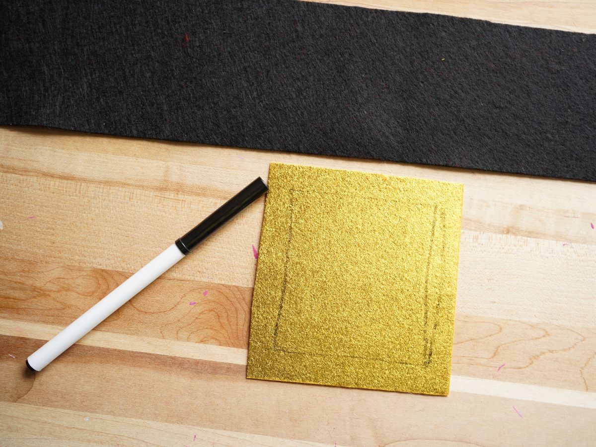 sheet of black felt cut into santa belt strip and gold felt cut into square with smaller inner square drawn on with marker