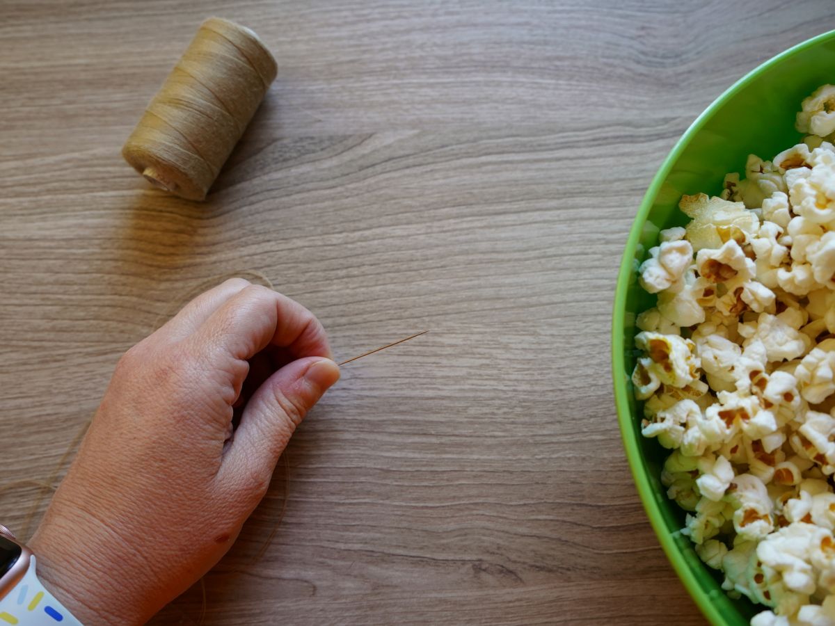 woman's hand with needle and thread through needle and bowl of popcorn