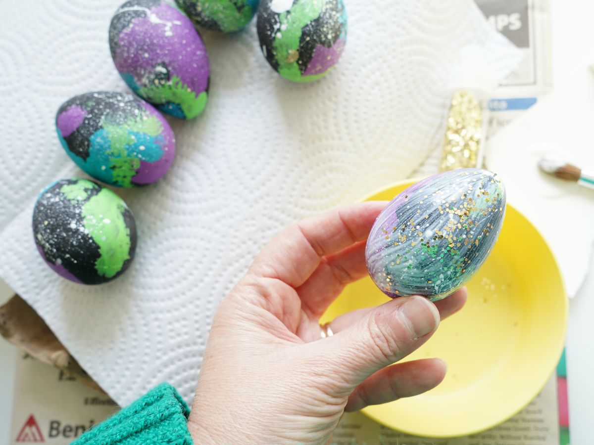 woman holding mod podge coated easter egg with gold glitter