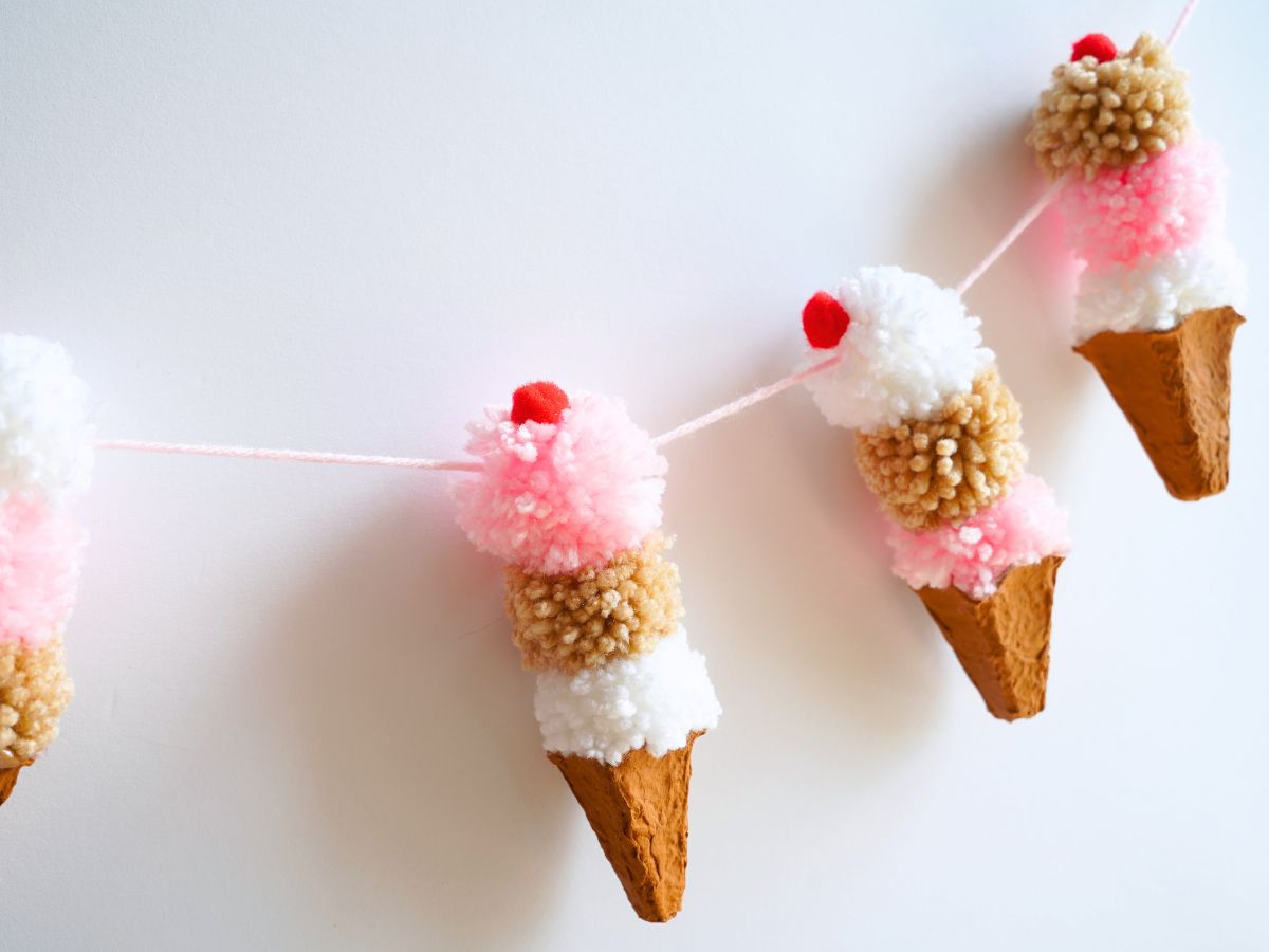 close up of pompom ice cream cone garland hanging on wall. 3 ice cream scoops on each cone