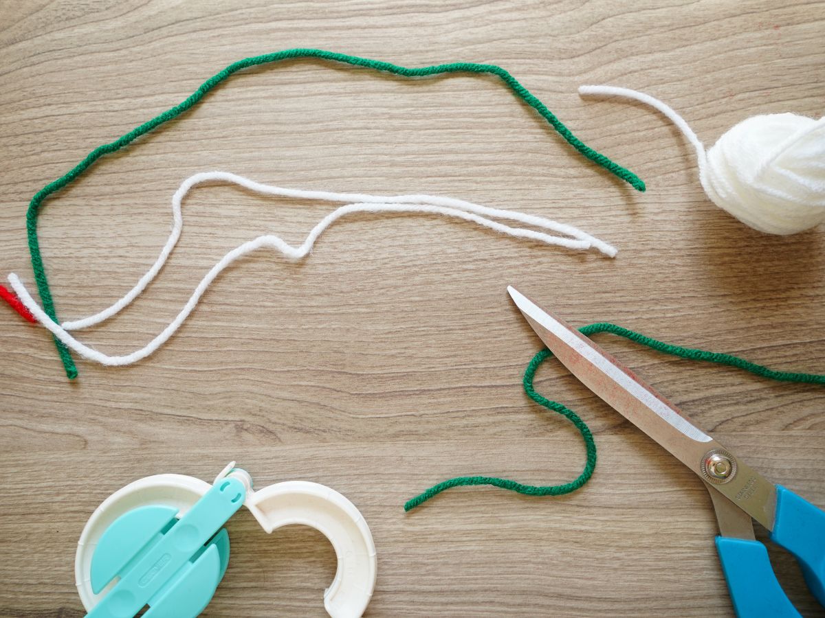 cut green and white yarn with scissors and clover pom pom maker tool