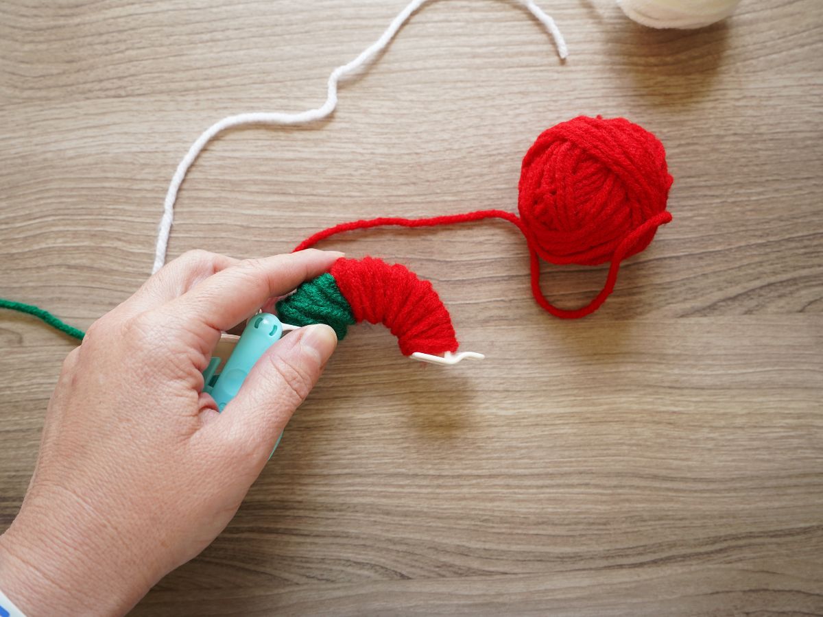 half of pom pom maker tool wrapped with green, red and white yarn for strawberry pom pom