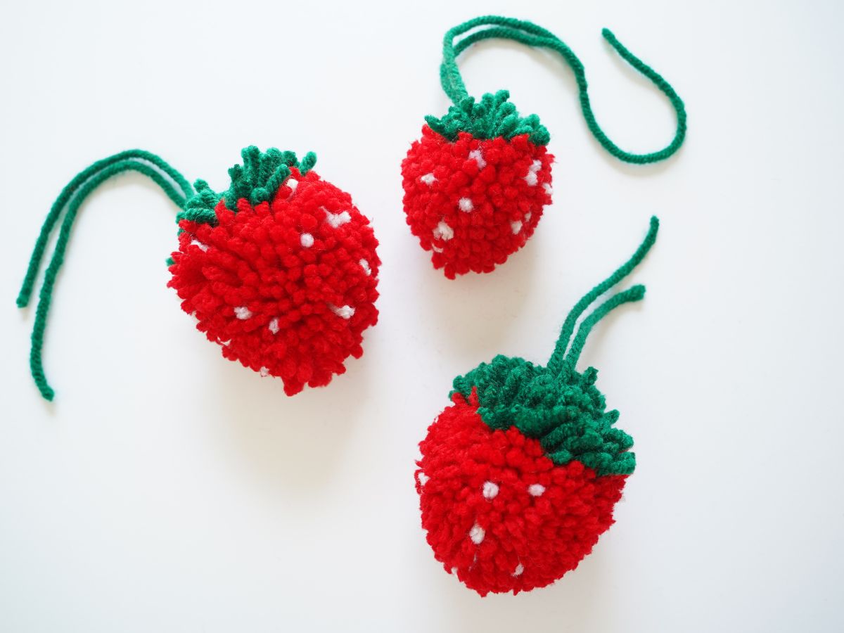one small and two large diy pom pom strawberries on white table