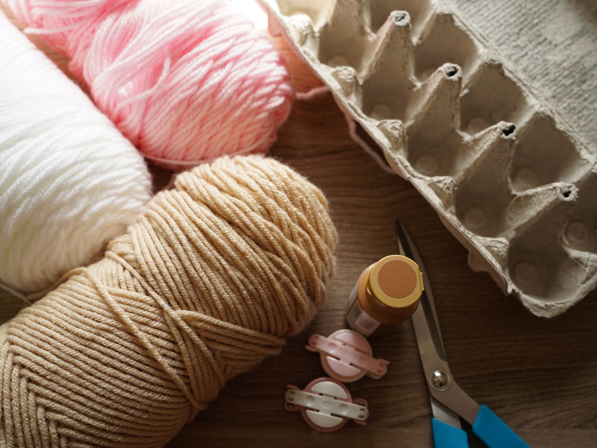 supplies for making ice cream cone pompoms - yarn, egg carton, paint scissors and pompom maker tool