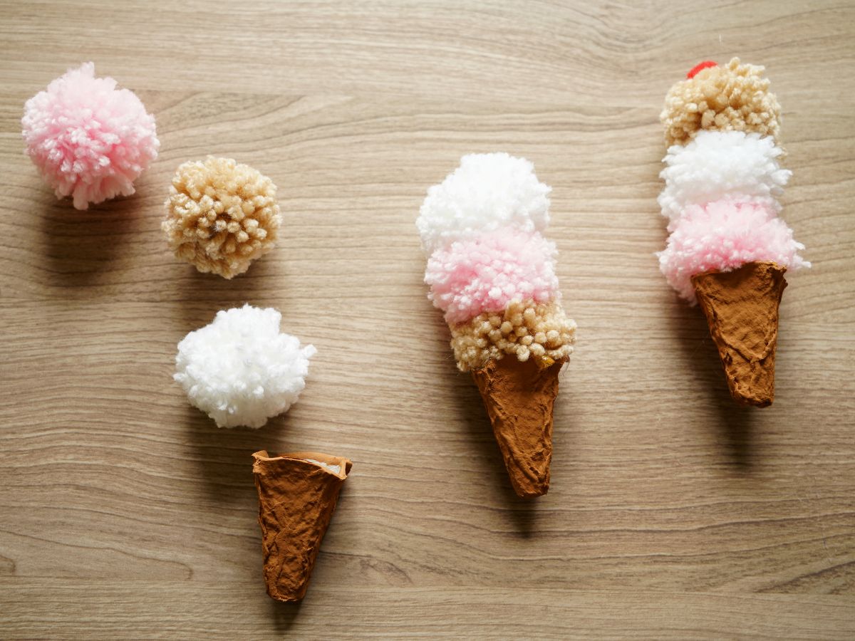 two finished diy pompom ice cream cones on table with one in pieces