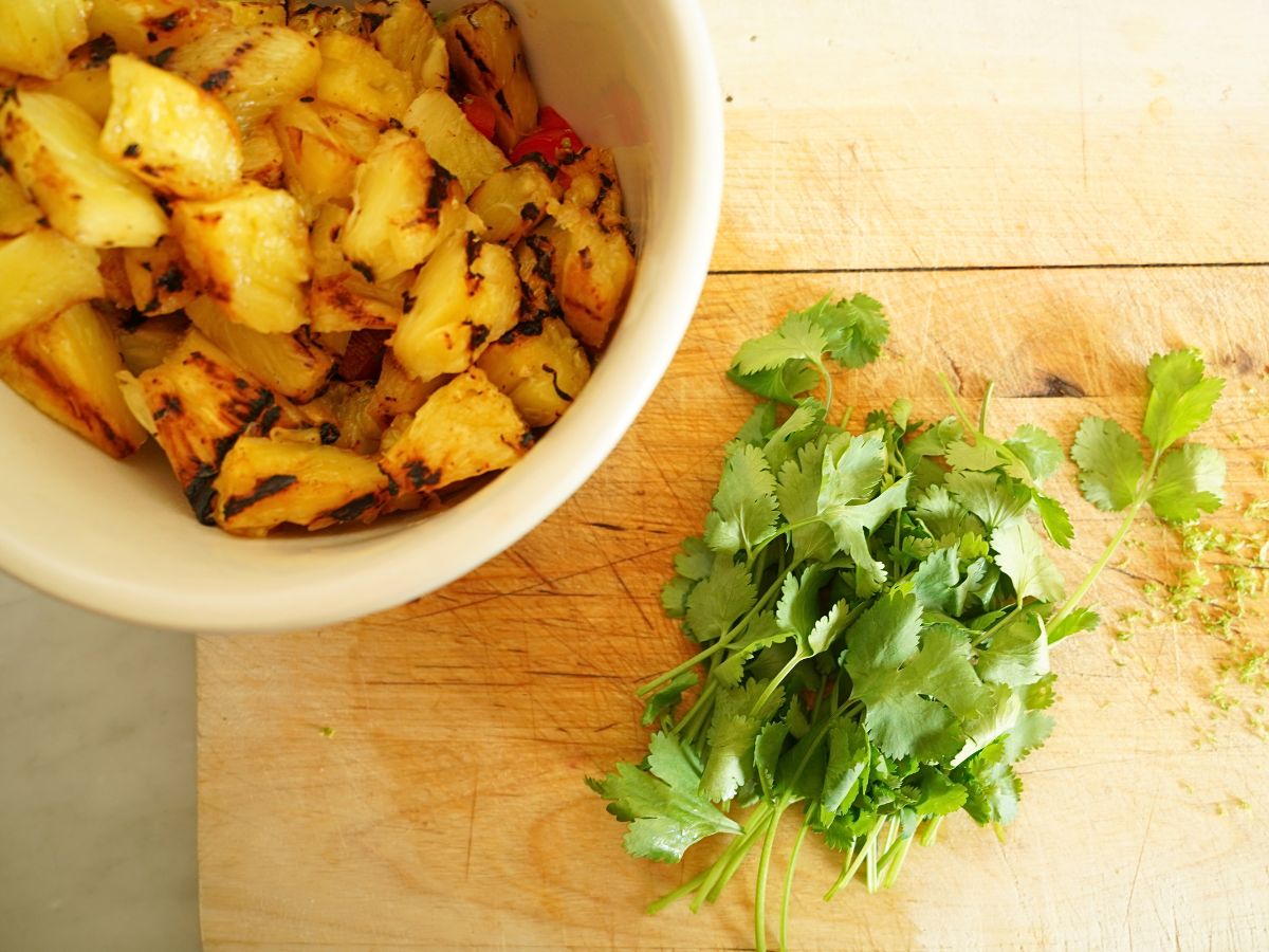 bowl of diced grilled pineapple and pile of cilantro on cutting board