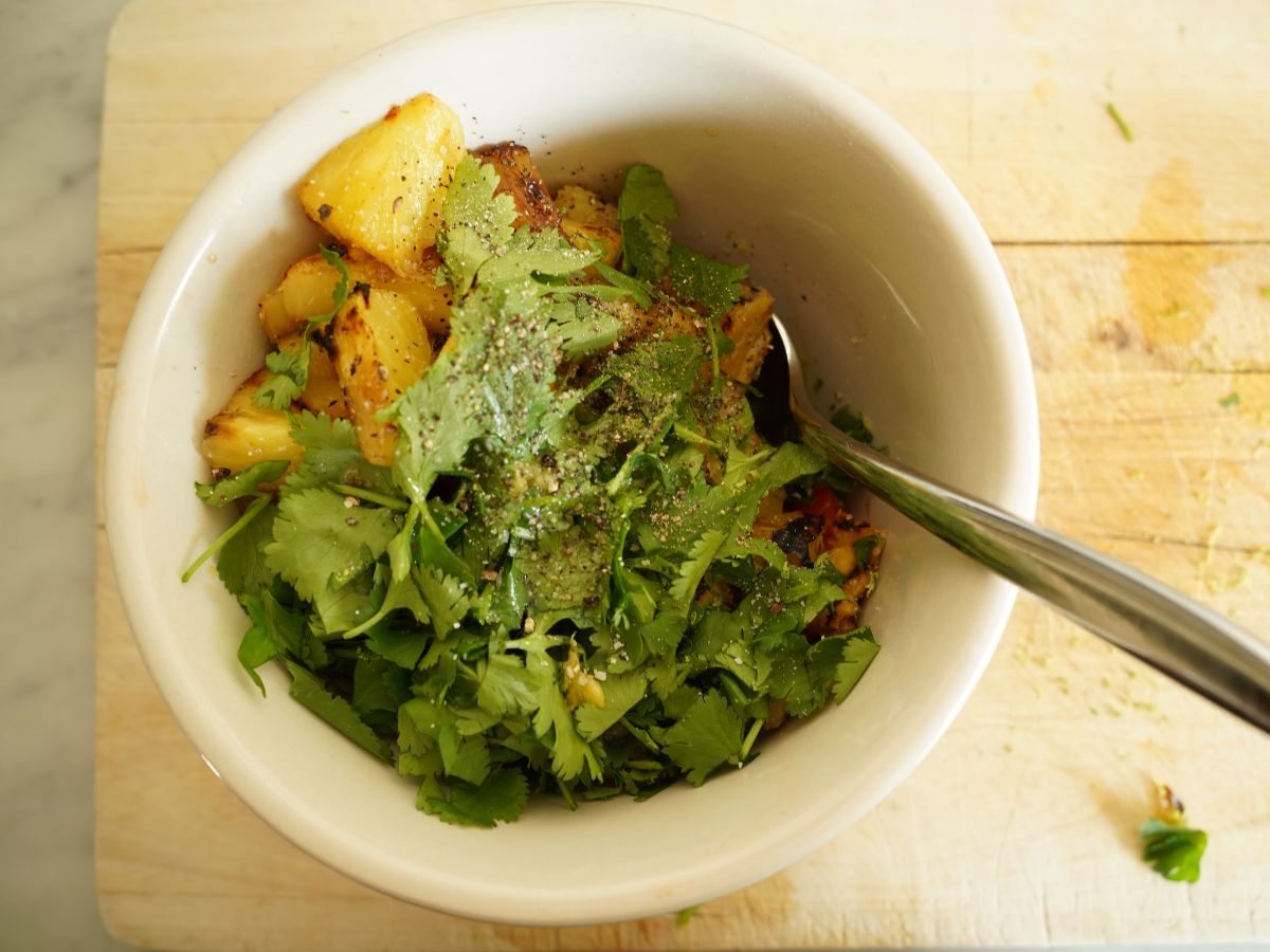 bowl with diced grilled pineapples, diced red peppers, cilantro, salt and pepper and a spoon
