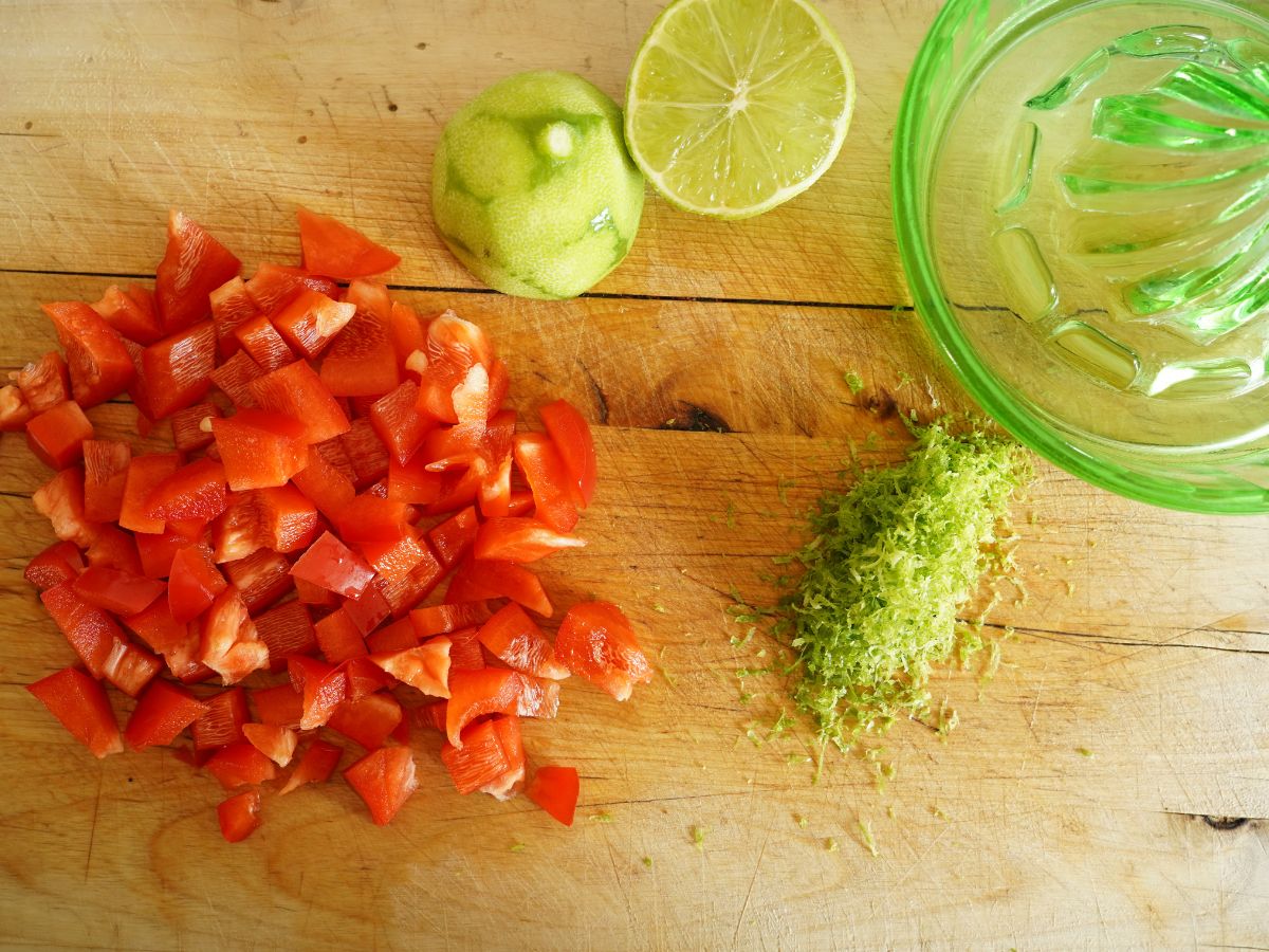 pile of diced red pepper and pile of lime zest with limes and juicer on cutting board