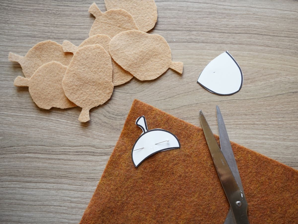 acorns being cut from brown felt sheets with template pinned to felt