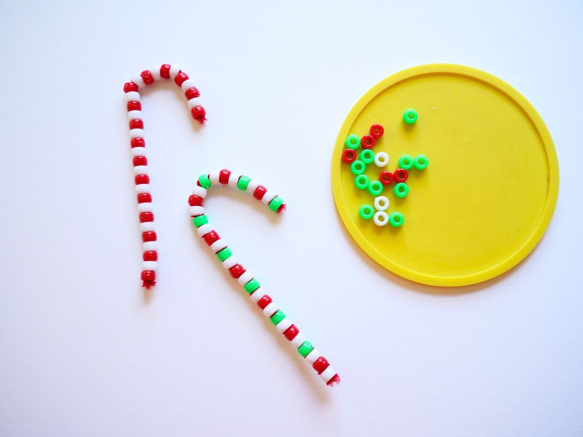 2 beaded pipe cleaner candy canes in traditional candy cane Christmas colors with pile of beads beside