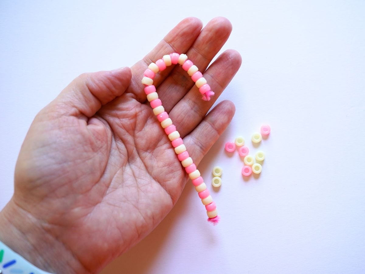 woman's hand holding pink and cream pipe cleaner candy cane