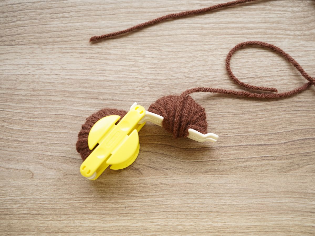 brown yarn wrapped around pom pom making tool