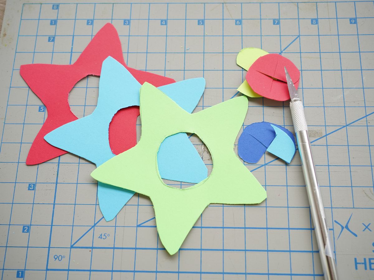 colorful cardstock cut into stars with holes in middle with craft knife and self healing mat