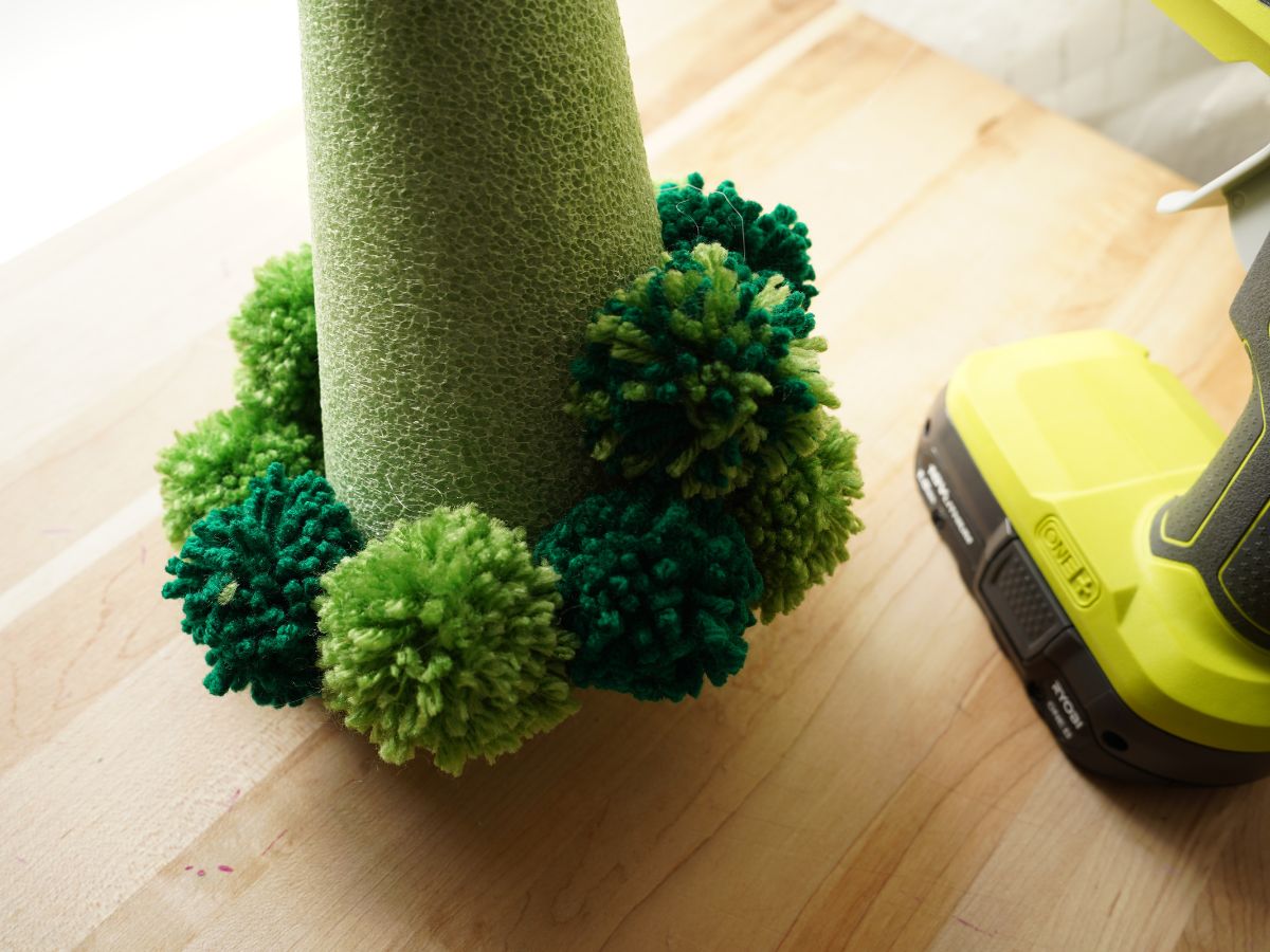 green pom poms being glued on green foam cone with glue gun