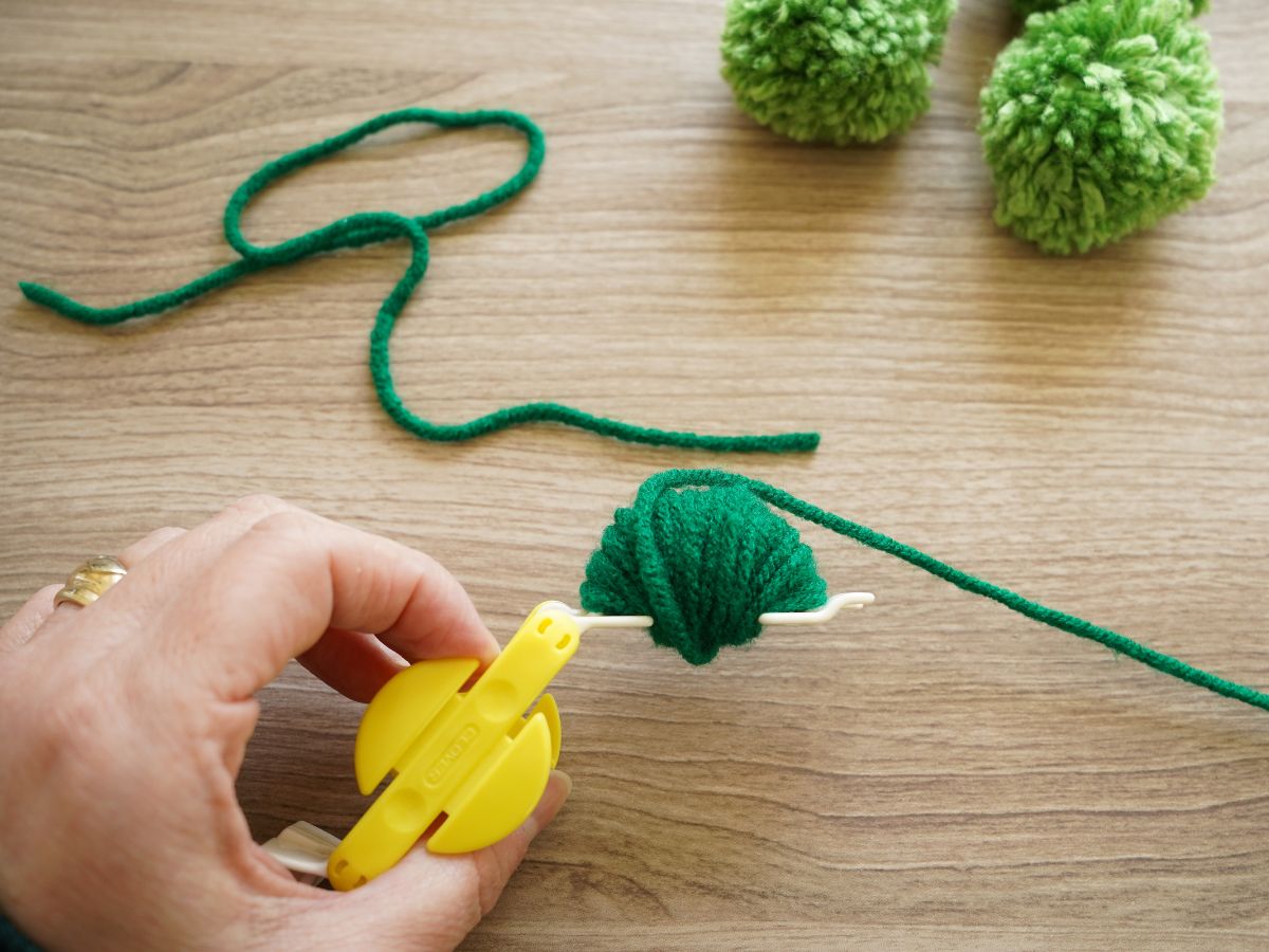 green yarn wrapped around one side of clover pom pom maker tool