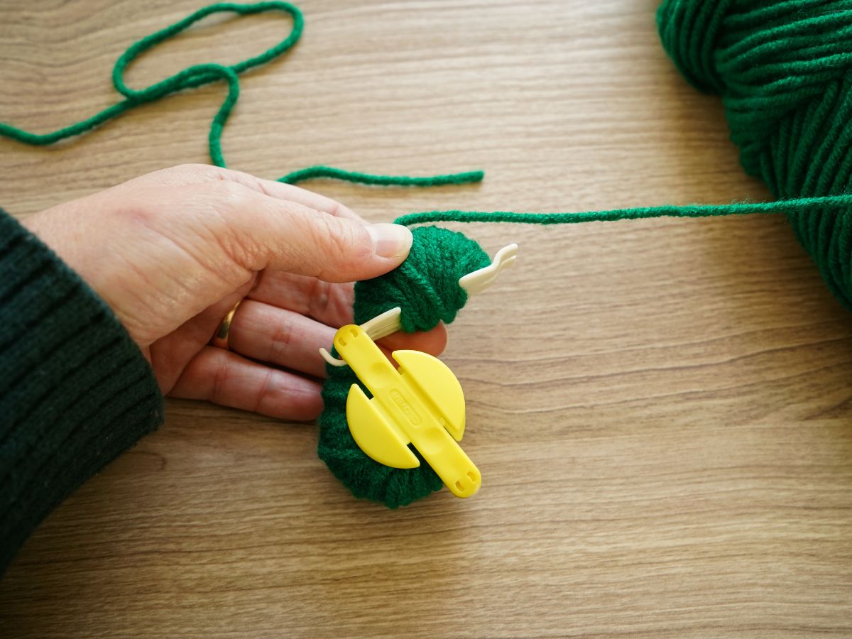 green yarn wrapped around two sides of pom pom maker tool in woman's hand