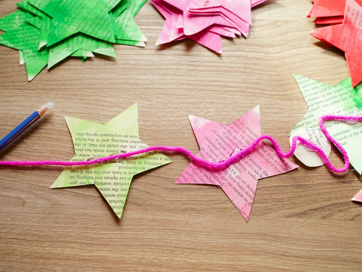 image of green and pink painted stars made from pages of a book being hot glued to a strand of pink yarn