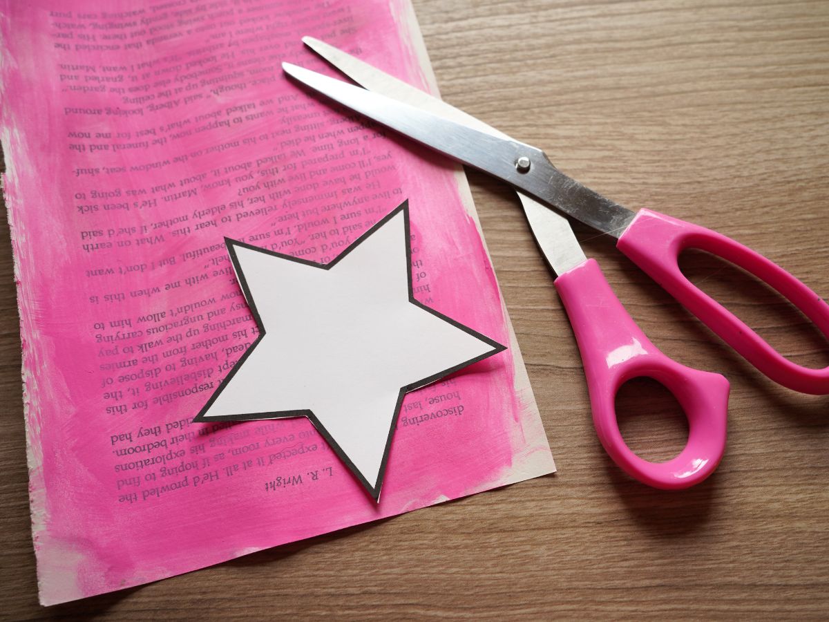image of star template cut out and sitting on a book page that is painted pink and a pair of scissors