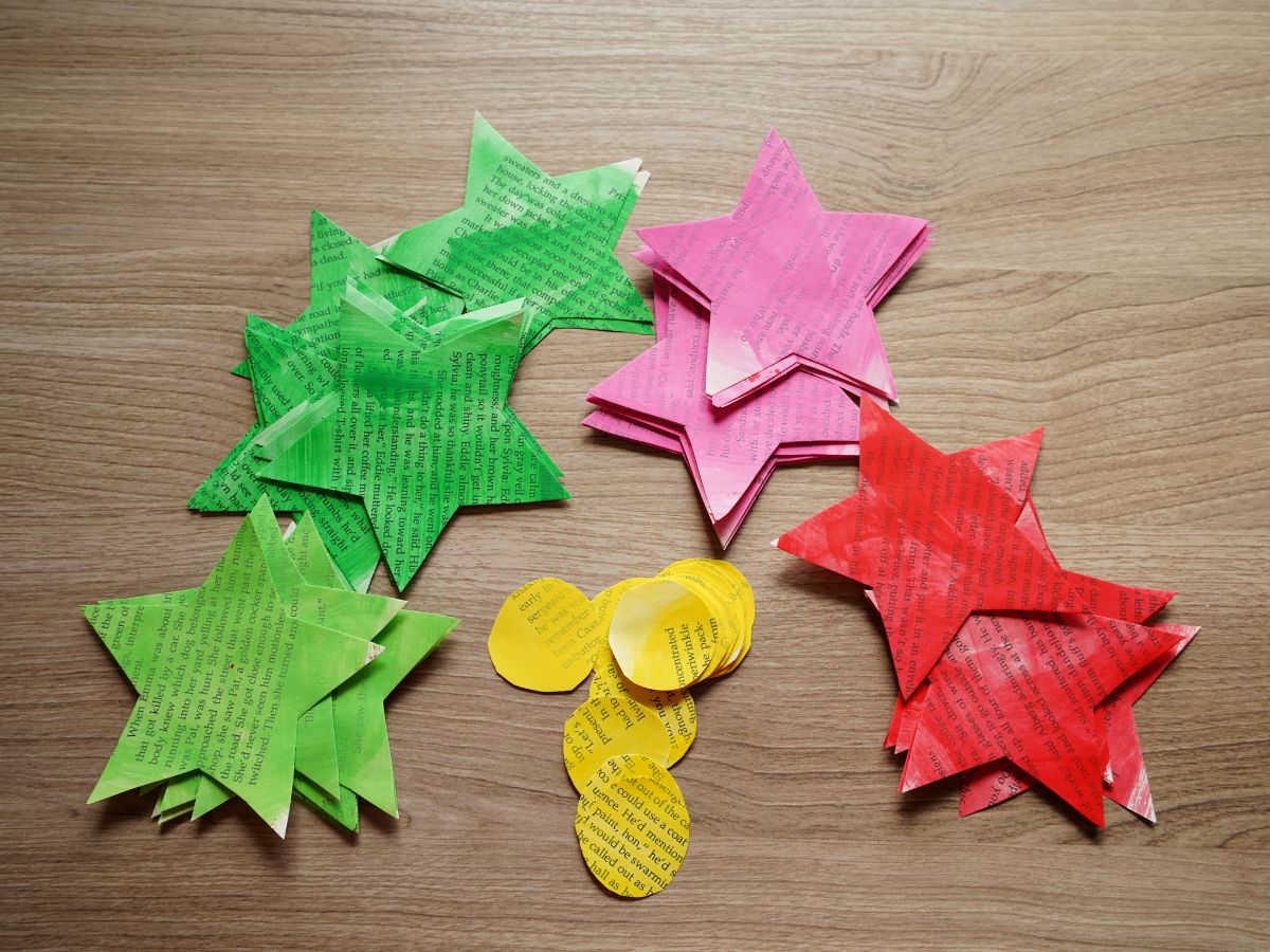 piles of light green, dark green, pink, and red stars made from book pages and pile of yellow circles cut from book pages