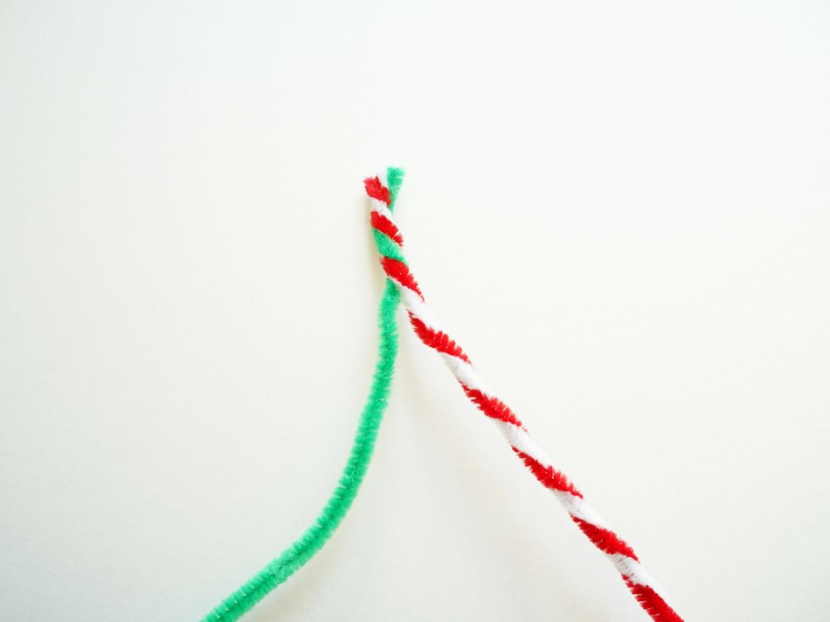red and white pipe cleaners twisted together with a green pipe cleaner being twisted onto them