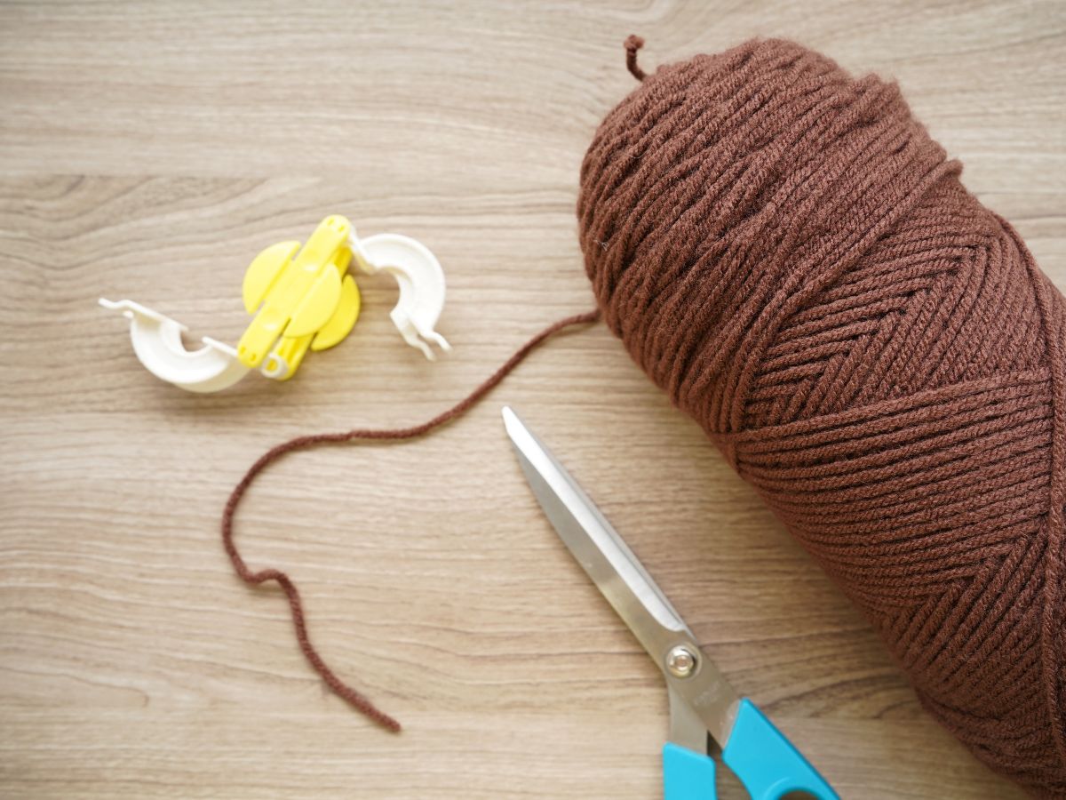 skien of brown yarn beside pom pom maker tool and pair of scissors