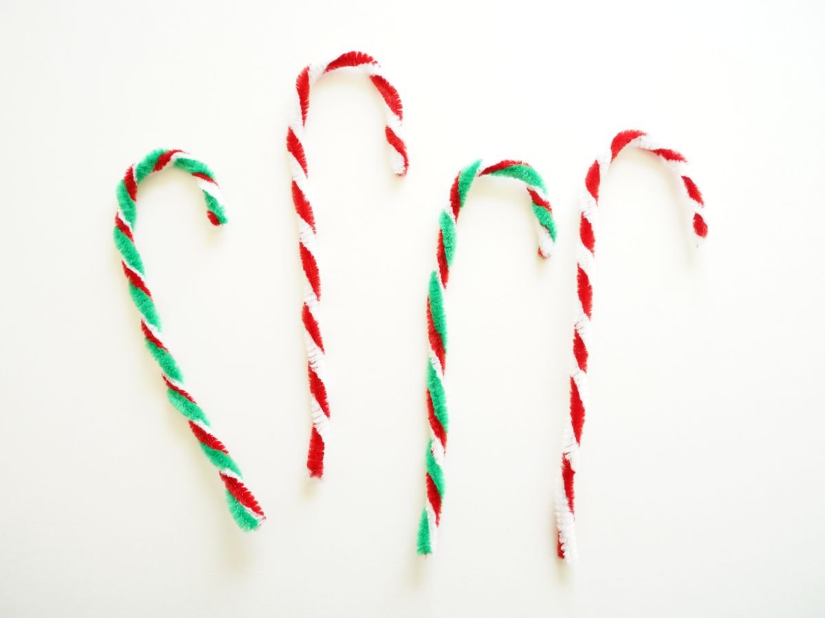 two red and white candy canes made from pipe cleaners and two red, white and green candy canes made from pipe cleaners on table