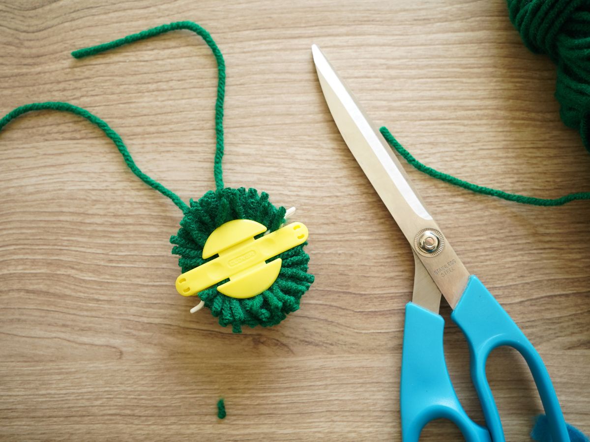 unopened clover pom pom maker tool with trimmed green yarn and pair of scissors