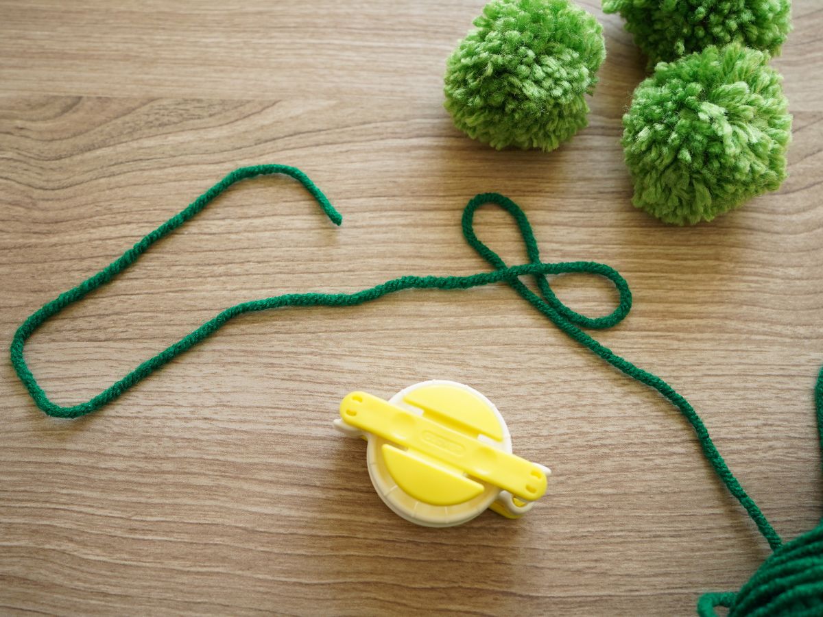 yellow pom pom maker tool with strand of green yarn beside it