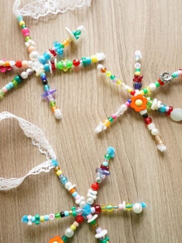 3 beaded pipe cleaner snowflakes with long lace ribbons on table