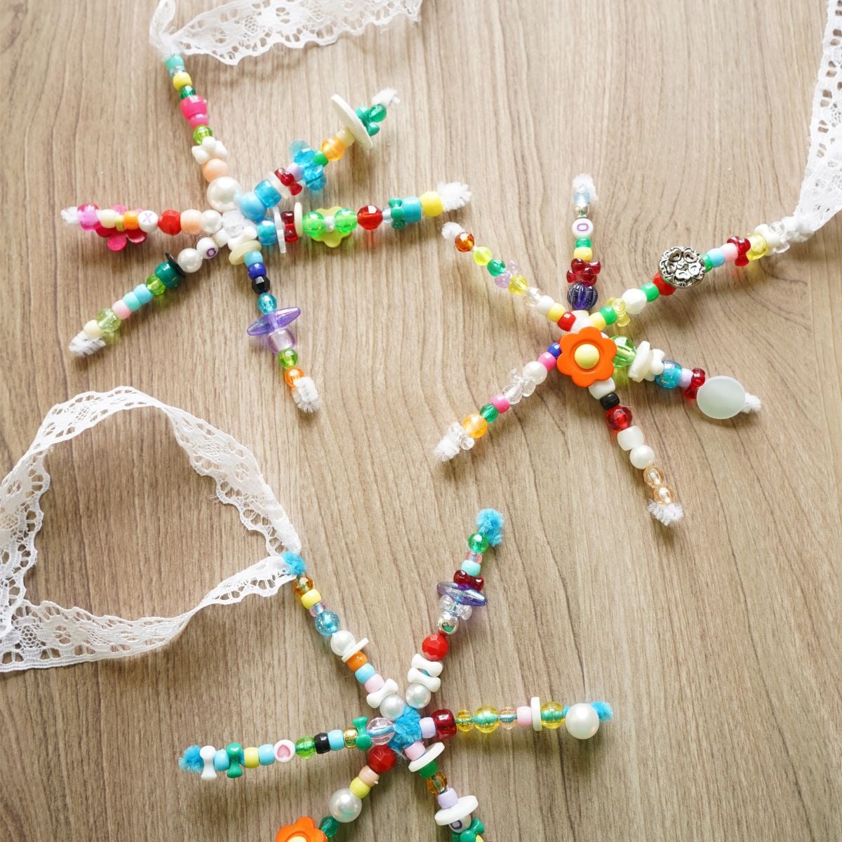 3 beaded pipe cleaner snowflakes with long lace ribbons on table