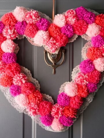 diy pink pom pom heart wreath hanging on door