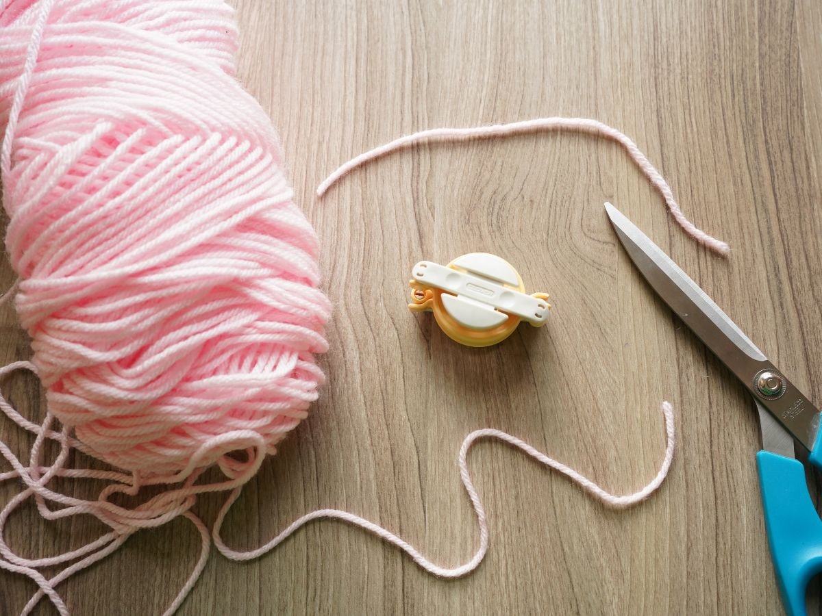 empty pom pom making tool with pink yarn and scissors