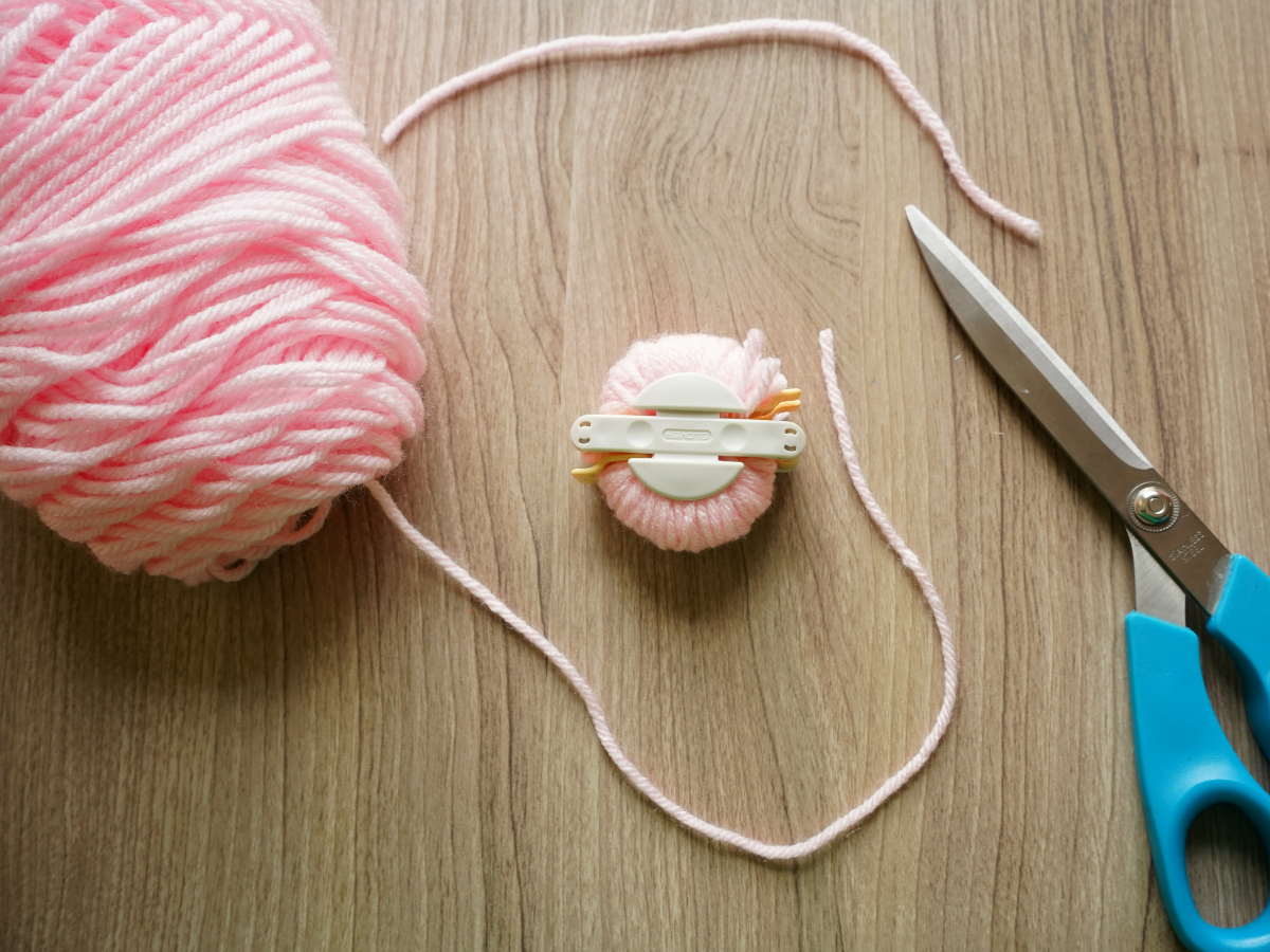 fully wrapped and closed pom pom maker with pink yarn and pair of scissors
