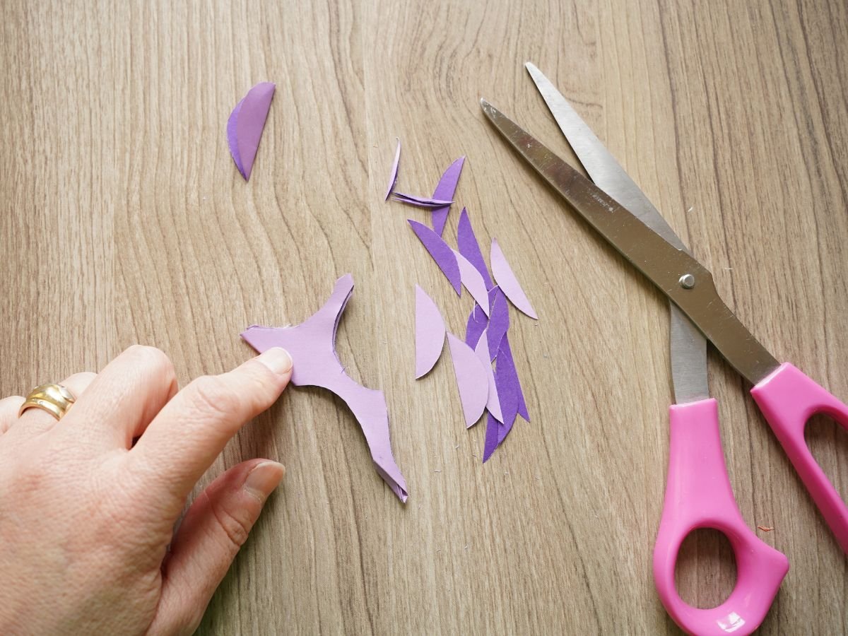 hand holding down paper snowflake cut out with pair of scissors