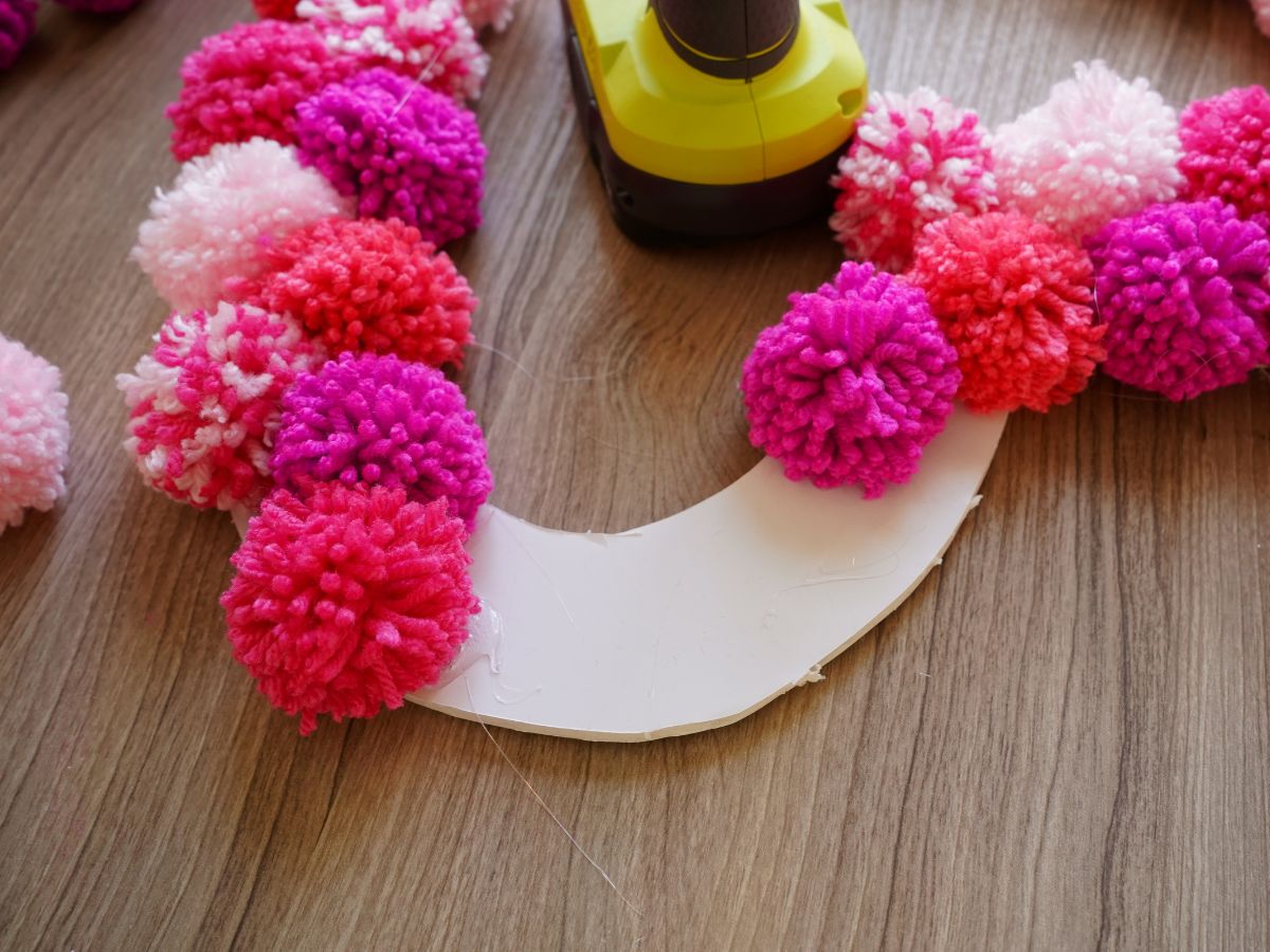 pom poms being glued onto foam core heart with glue gun