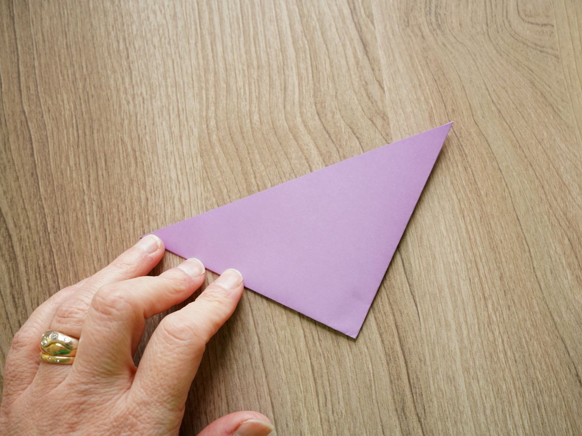 purple origami paper folded in half again with hand pressing fold