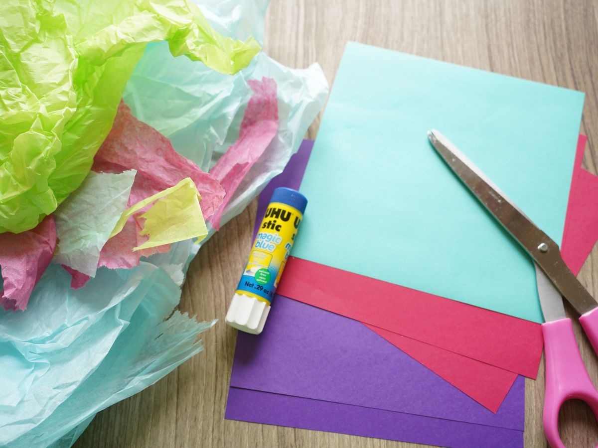 supplies needed to make paper snowflake sun catcher craft - tissue paper, glue stick, scissors and origami paper