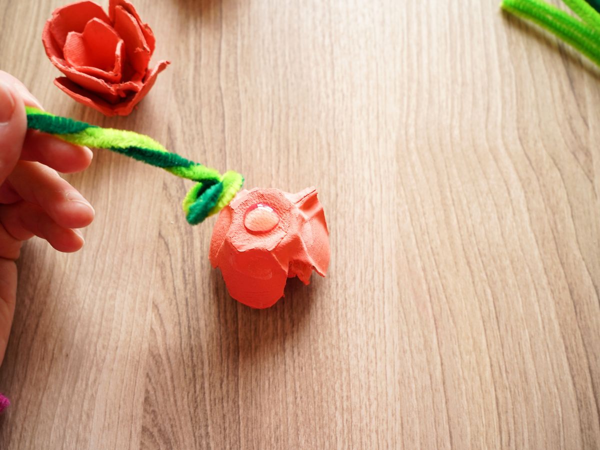 pipe cleaner flower stem being pressed into dollop of hot glue on back of egg carton rose