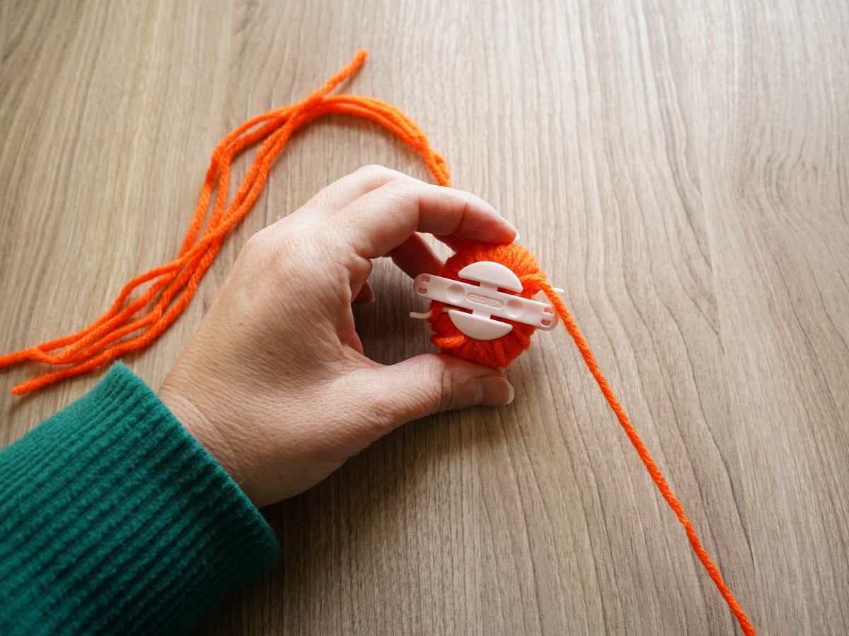 both sides of pom pom maker wrapped with orange yarn and closed in hand