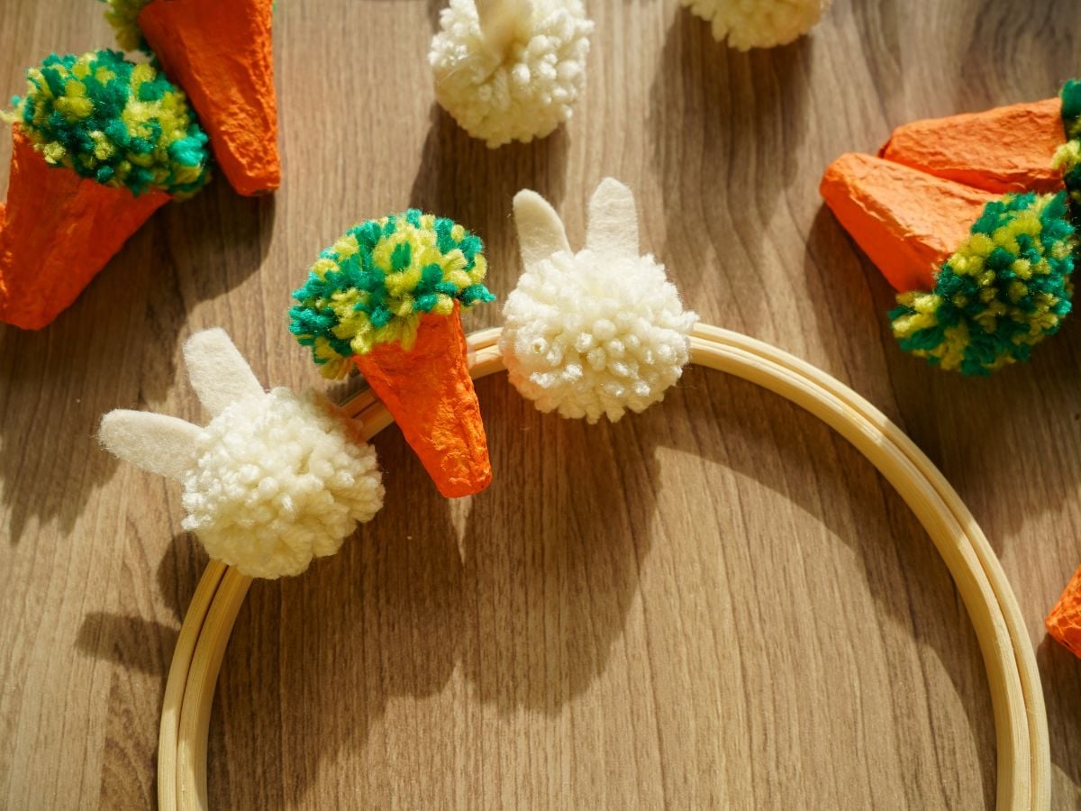 close up of pom pom bunnies glued onto embroidery hoop with egg carton carrot