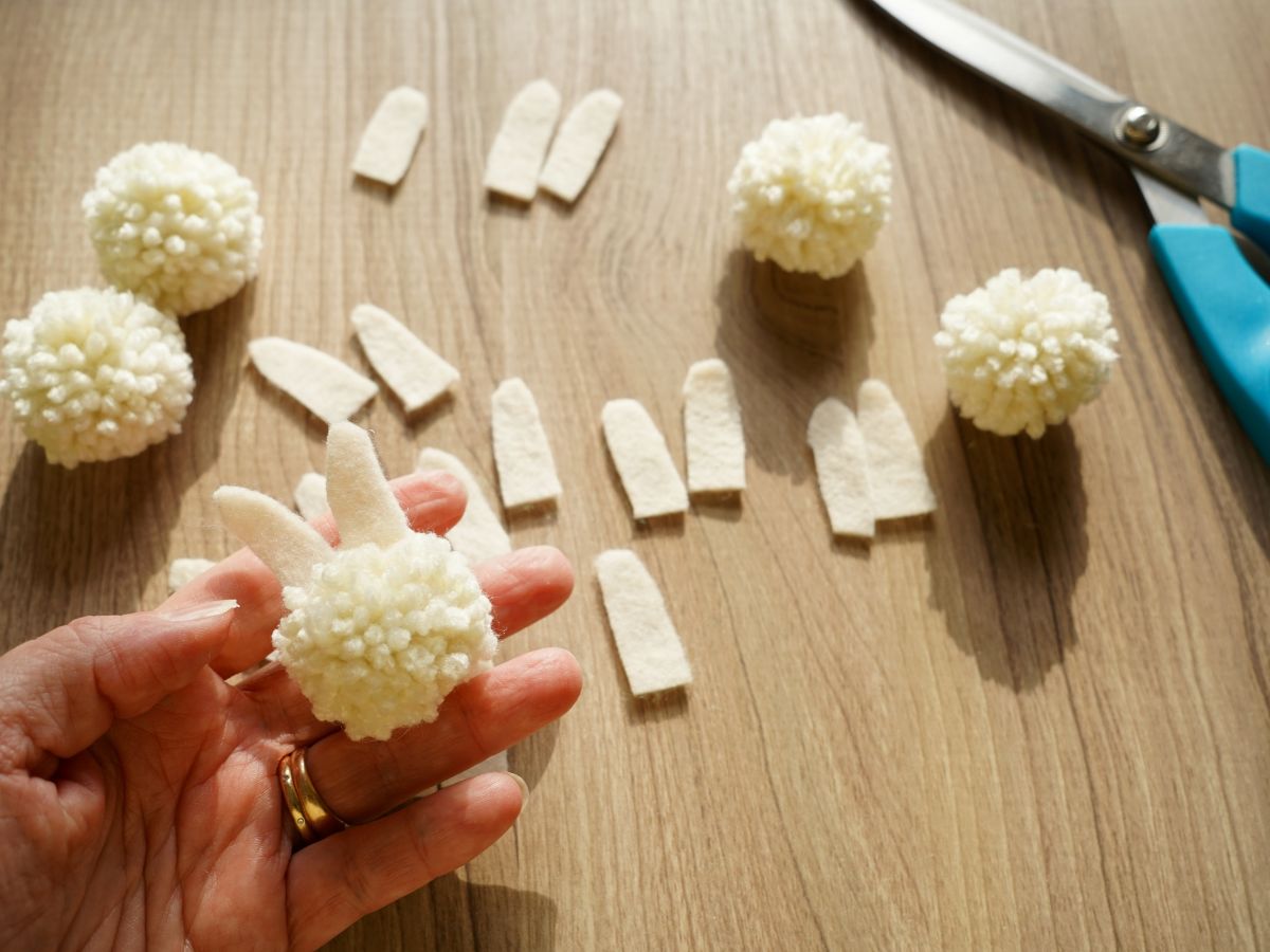cream colored yarn pom poms with bunny ears cut from cream felt and pair of scissors