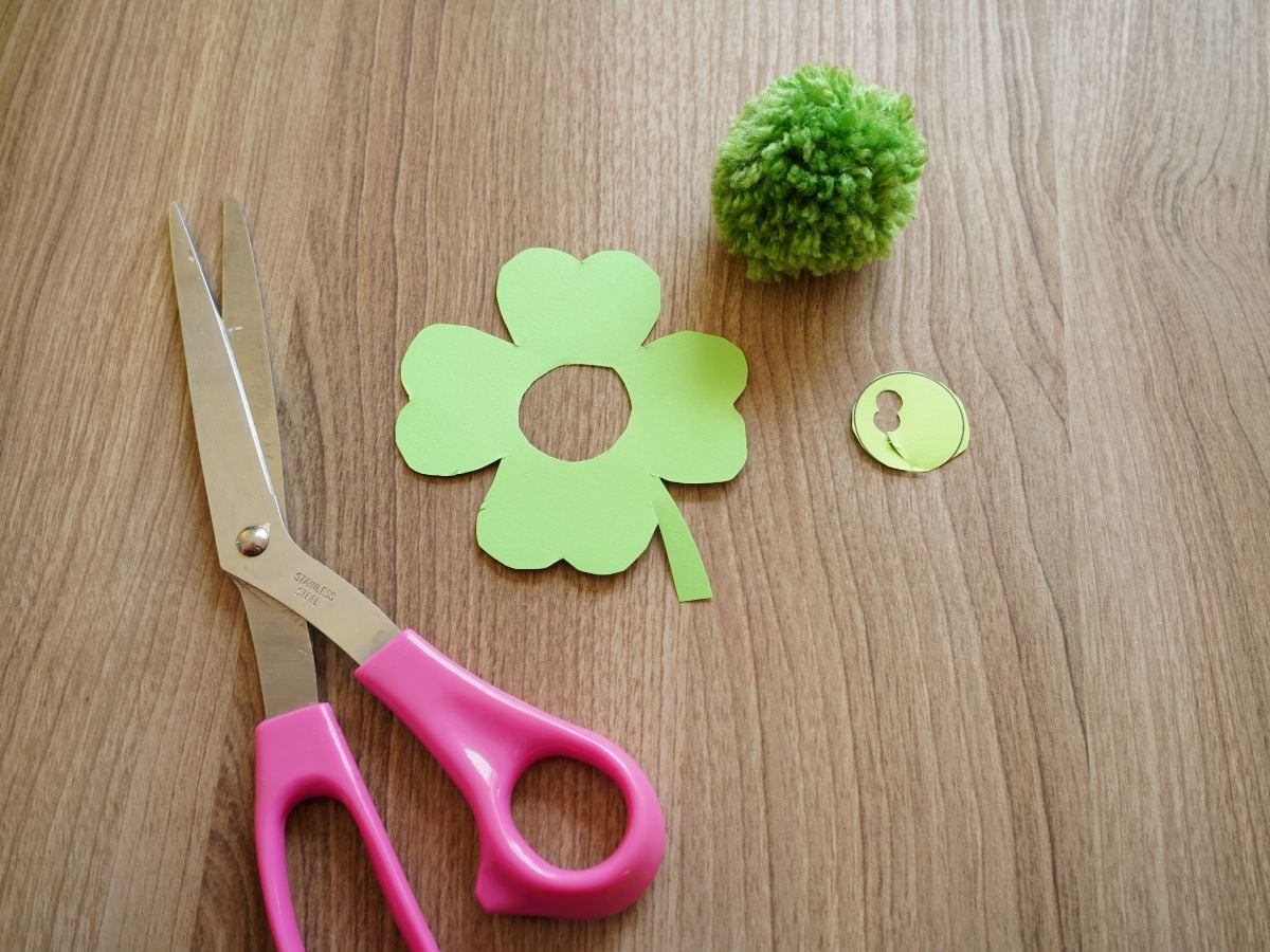 hole cut from centre of paper four leaf clover with pair of scissors and green pom pom