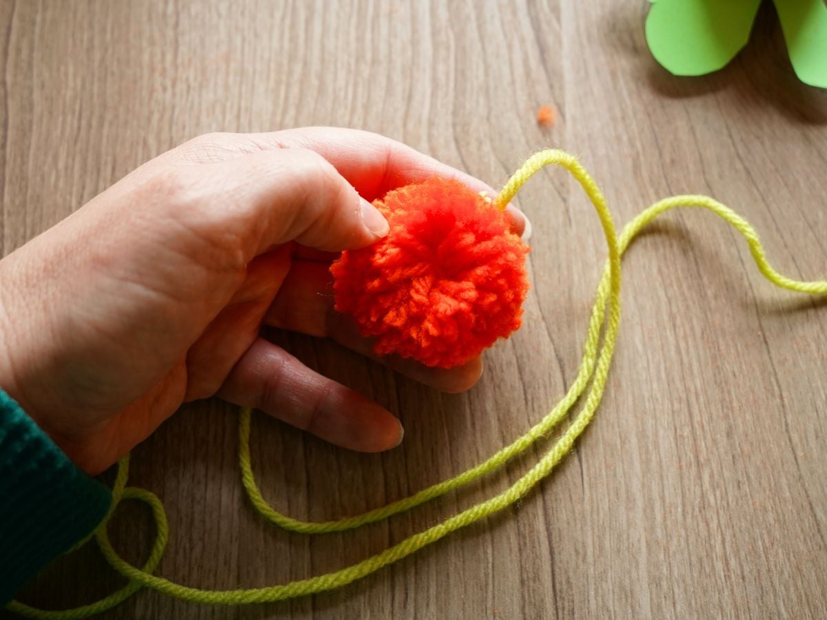 orange pom pom in hand showing centre string in the middle of the pom pom