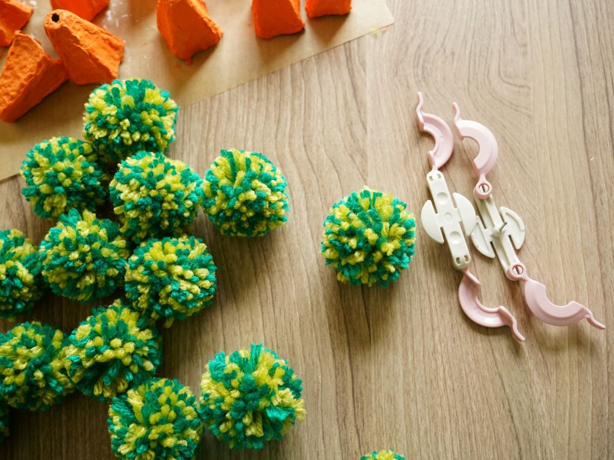 pile of carrot top pom poms on table made from two shades of green yarn