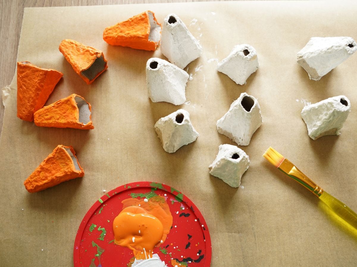 pile of egg carton pieces painted white and orange with paint brush on table